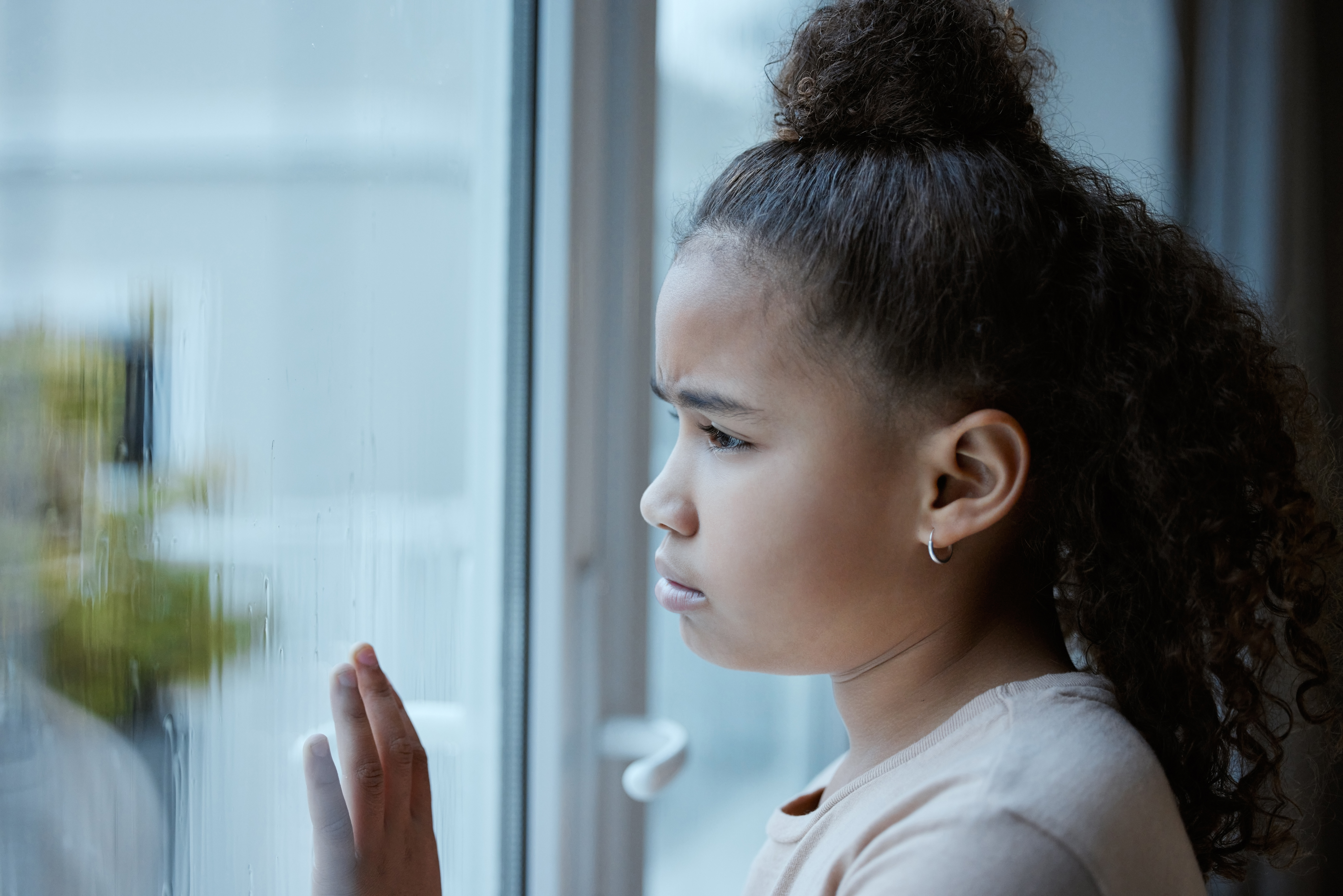 Shot of a little girl starting out of the window looking sad at home